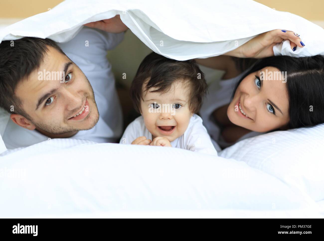 Happy family posing under a duvet while looking at the camera Stock