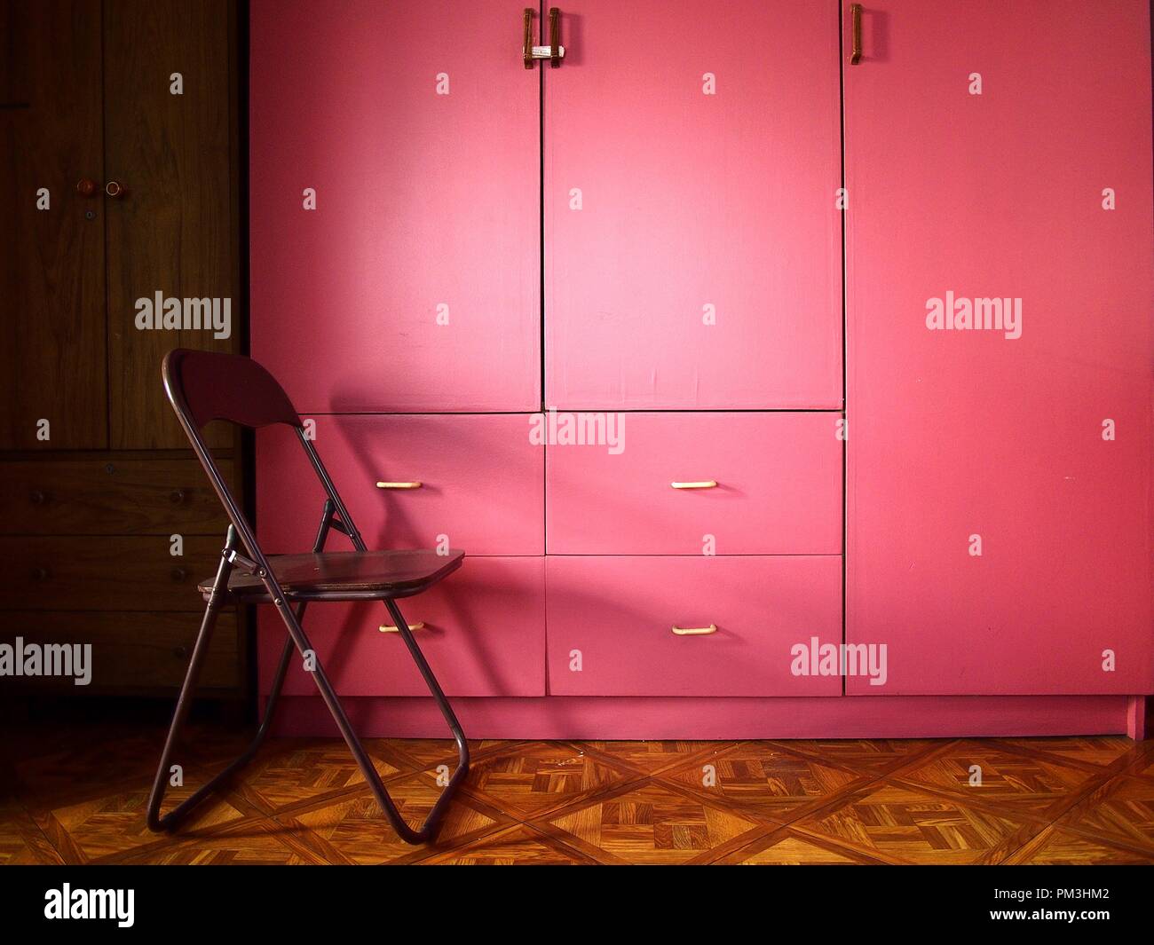 Photo of a pink colored wooden cabinet or closet in a room and a chair Stock Photo
