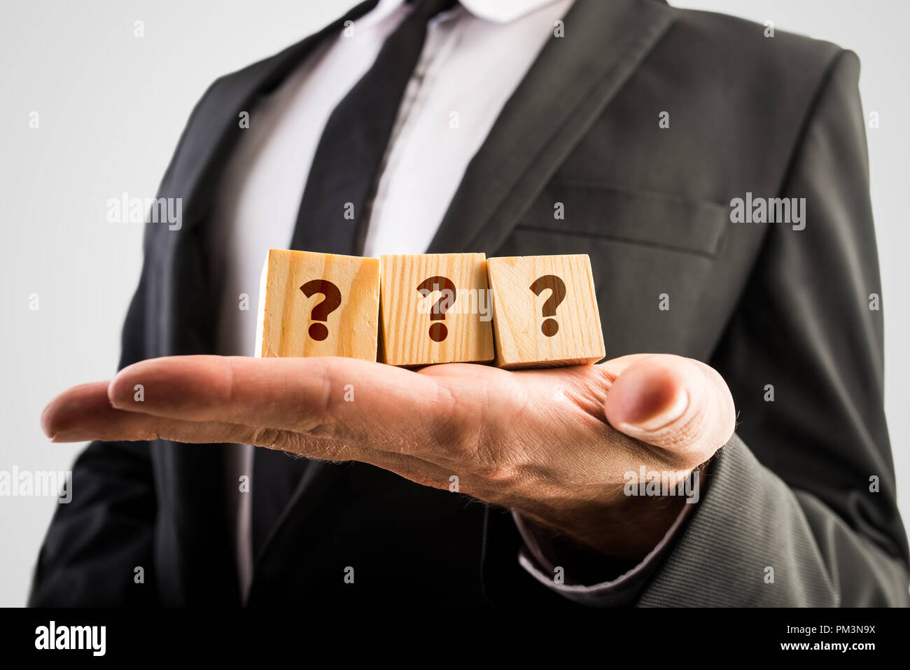 Businessman holding three wooden cubes displaying question marks. Stock Photo