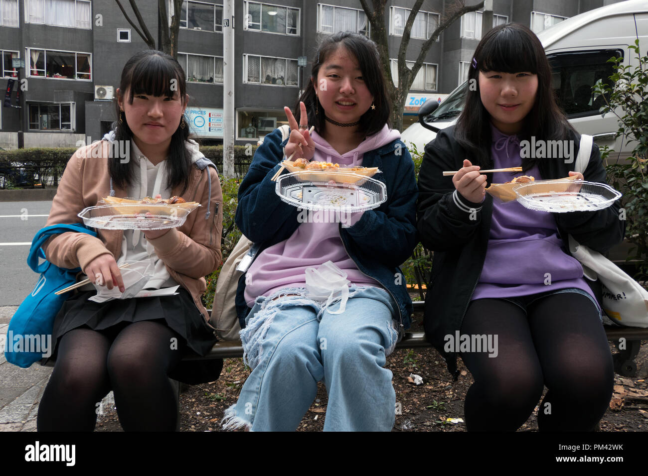 Three Japanese girls eating junk food on Omotesando street, Tokyo, Japan, Asia. Female friends having quick lunch Stock Photo