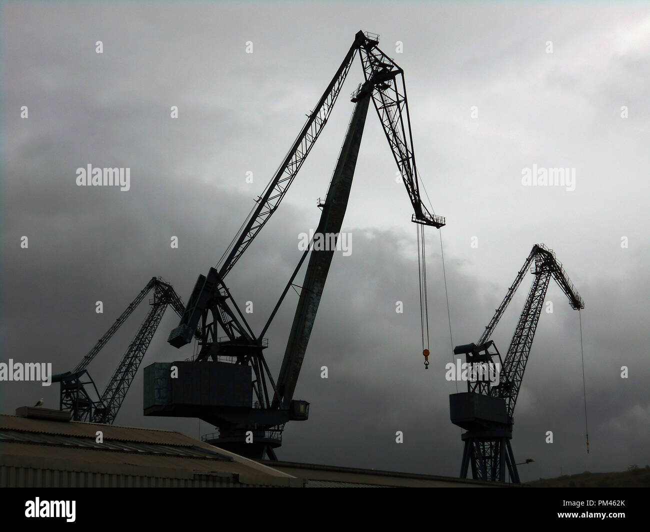 A few huge lifting, industrial cranes, sit silhouetted against a dark sky, like giant birds, on the quayside at Port Glasgow on the Firth of Clyde in Scotland. Stock Photo