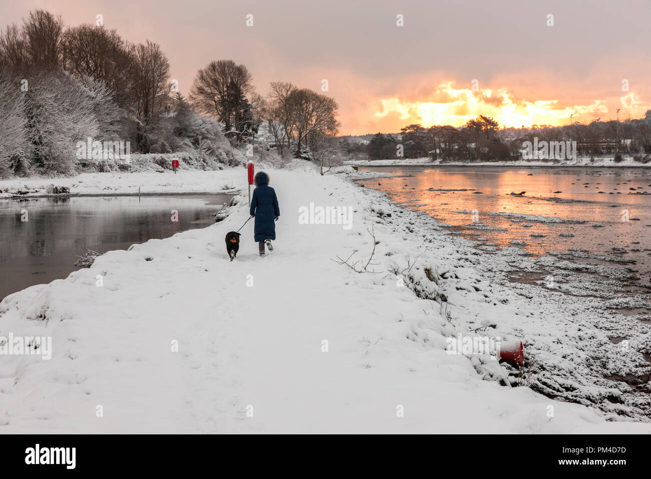 Carrigaline, Cork, Ireland. 28th February 2018. A woman walks her dog around the pond in the Community Park at dawn in Carrigaline Co. Cork, Ireland Stock Photo