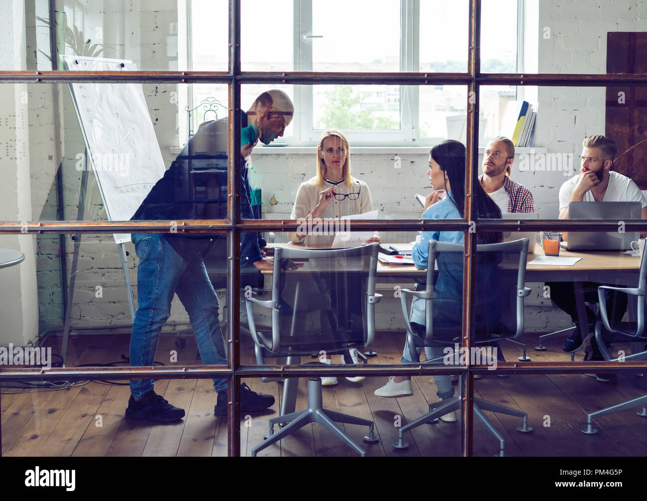 Young professional team. Group of young modern people in smart casual wear having a brainstorm meeting while standing behind the glass wall in the creative office. Stock Photo