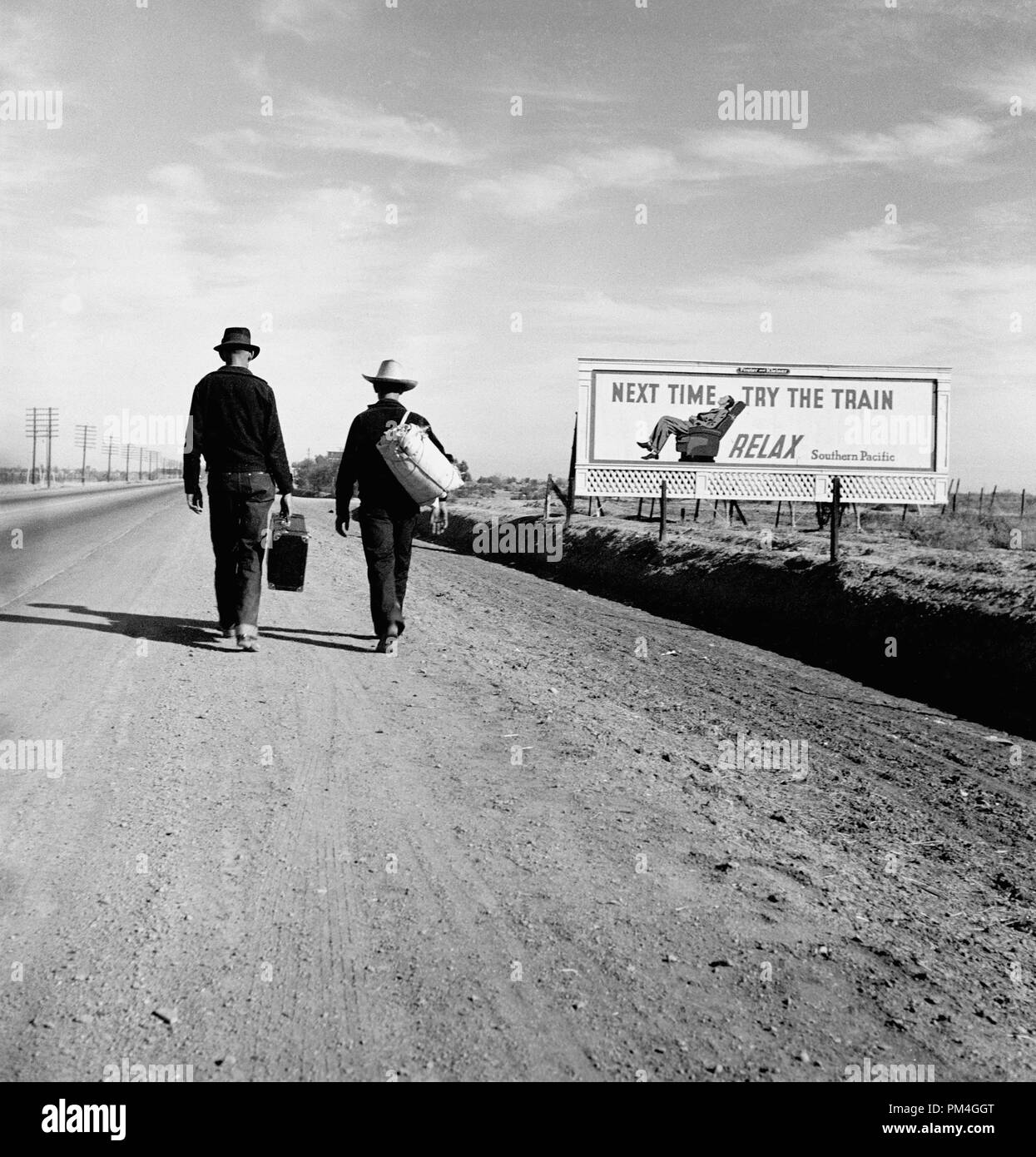 Two people (travelers) hitchhiking along road near a billboard that