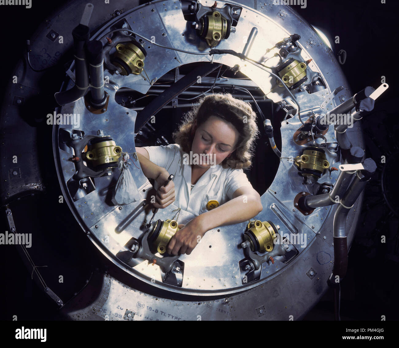 A woman worker concentrates on part of the cowling for one of the motors of a B-25 bomber being assembled in the engine department of North American (Aviation, Inc.'s) Inglewood, CA, plant, 1942.   File Reference # 1003 035THA Stock Photo
