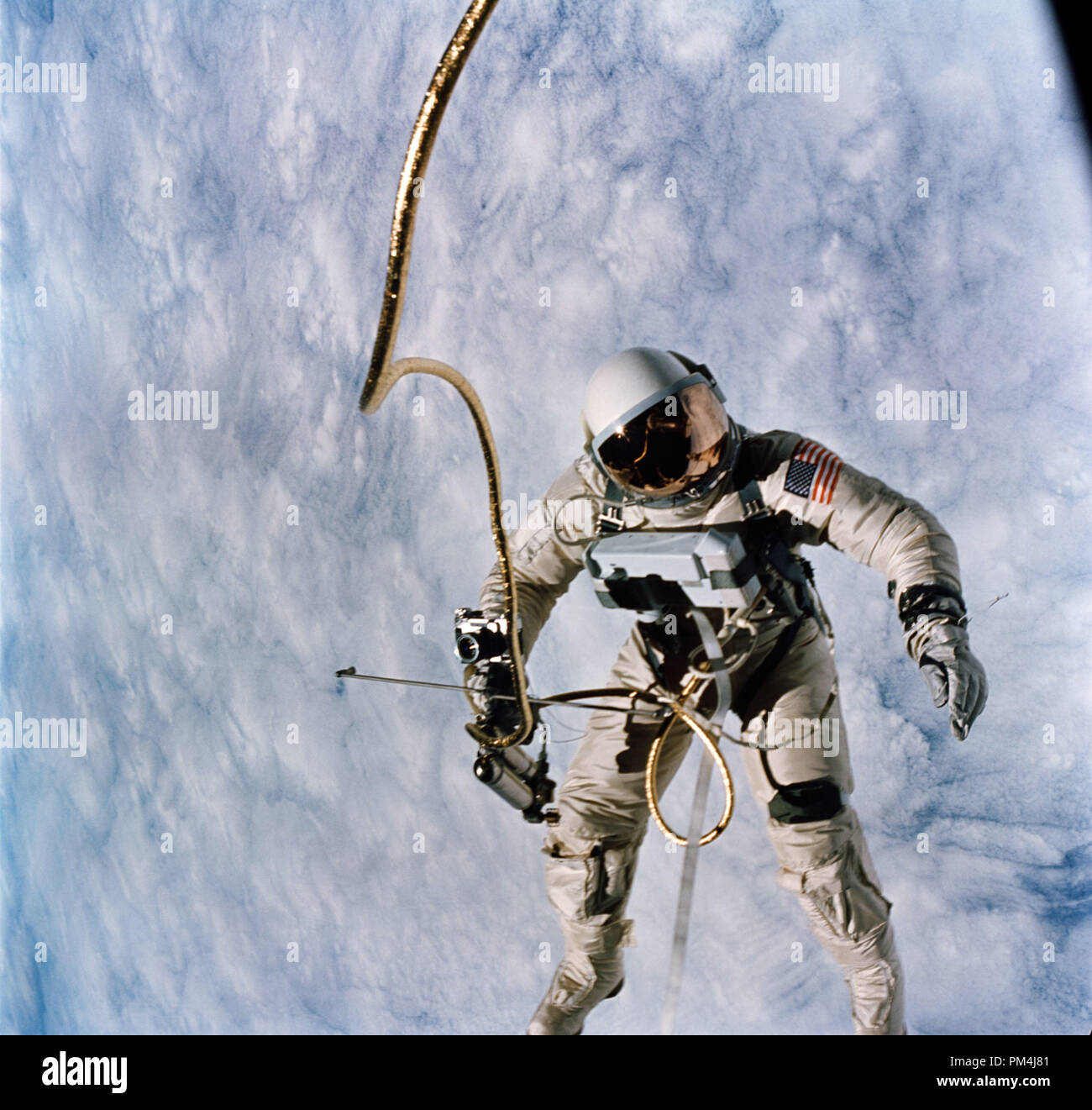 Astronaut Edward H. White, pilot for the Gemini IV spaceflight, floats in space during the first spacewalk by an American. The extravehicular activity, or spacewalk, was performed during the third Earth orbit of the Gemini IV mission. White is attached to the spacecraft by a 25-foot umbilical line and a 23-foot tether line, both wrapped in gold tape to form one cord. In his right hand White carries a Hand-Held Self-Maneuvering Unit. The visor of his helmet is gold-plated to protect him from the unfiltered rays of the sun. (June 3, 1965)   File Reference # 1003 592THA Stock Photo