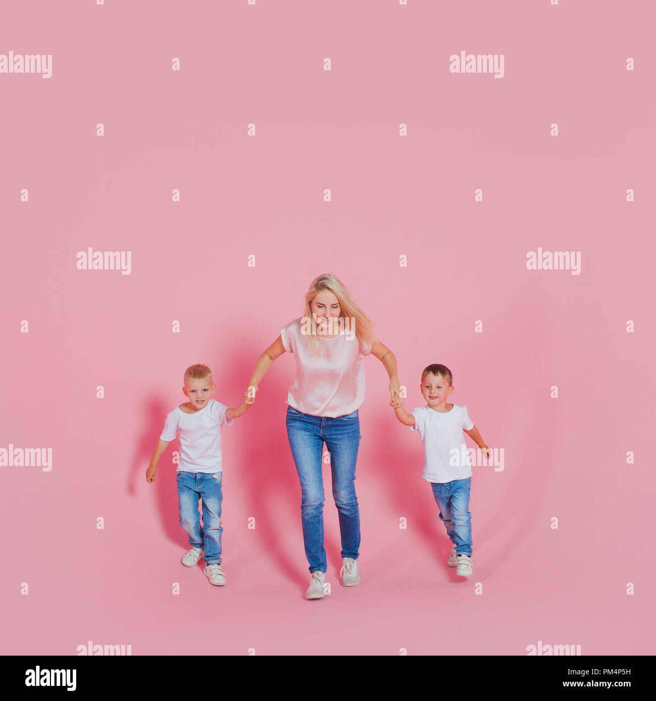 Beautiful blonde mom with two happy sons. Young woman and two baby boys, pink background Stock Photo
