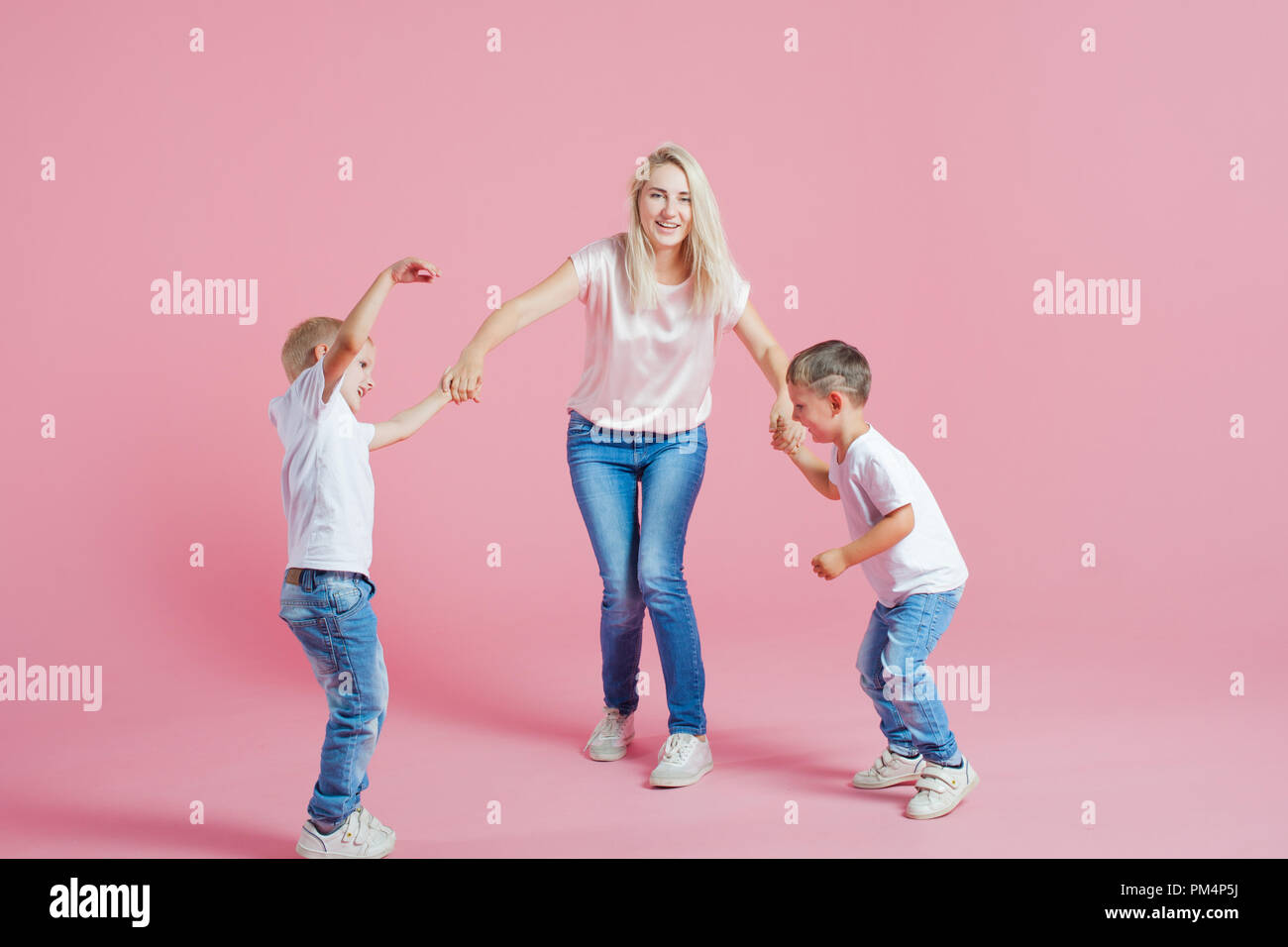 Beautiful blonde mom with two happy sons. Young woman and two baby boys, Jump and dance on pink background Stock Photo