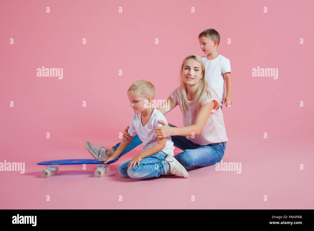 Beautiful blonde mom with two happy sons. Young woman and two baby boys, pink background Stock Photo