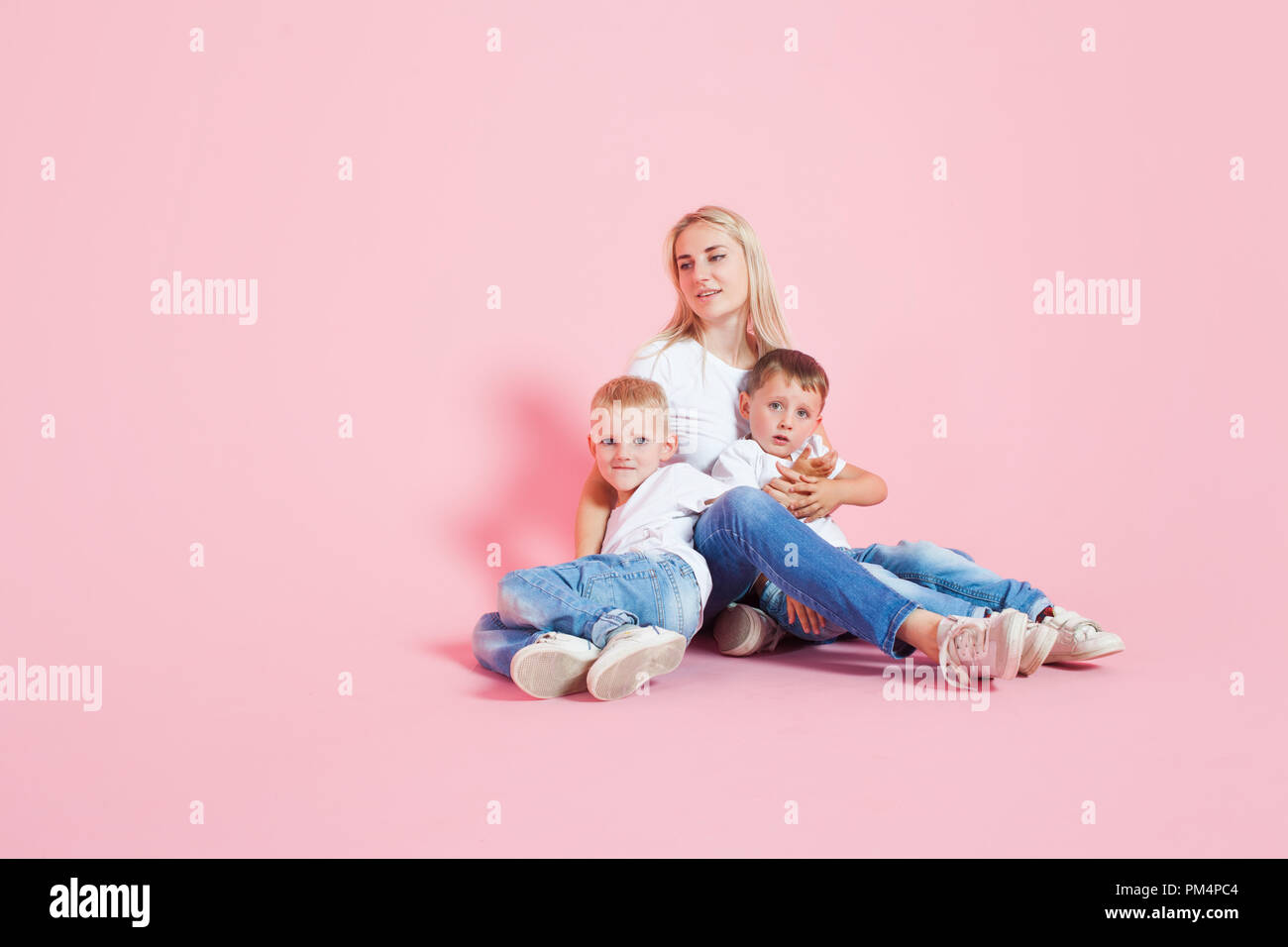 happy mom with two happy sons. Young woman and two baby boys, pink background Stock Photo