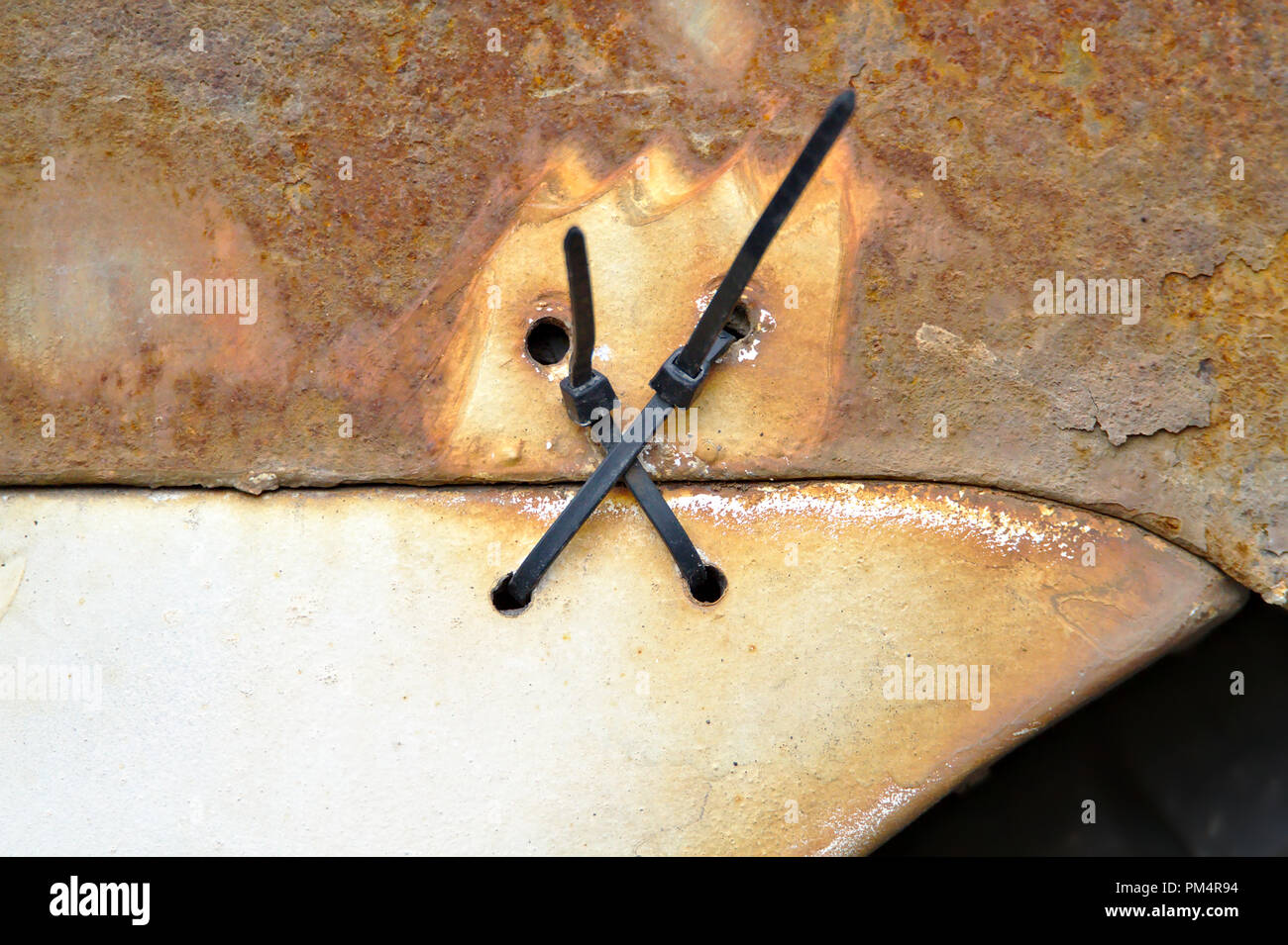 Detailed photo of two cable ties holding a rear bumper of old very rusty car. Stock Photo