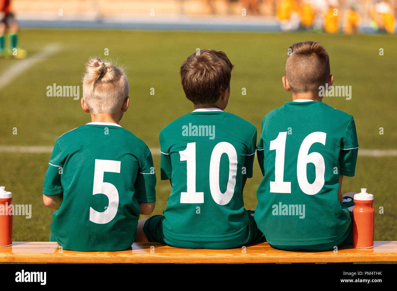 Kids Football Team. Soccer children watching game. Football soccer tournament match for children. Kids substitute players sitting on a wooden bench Stock Photo