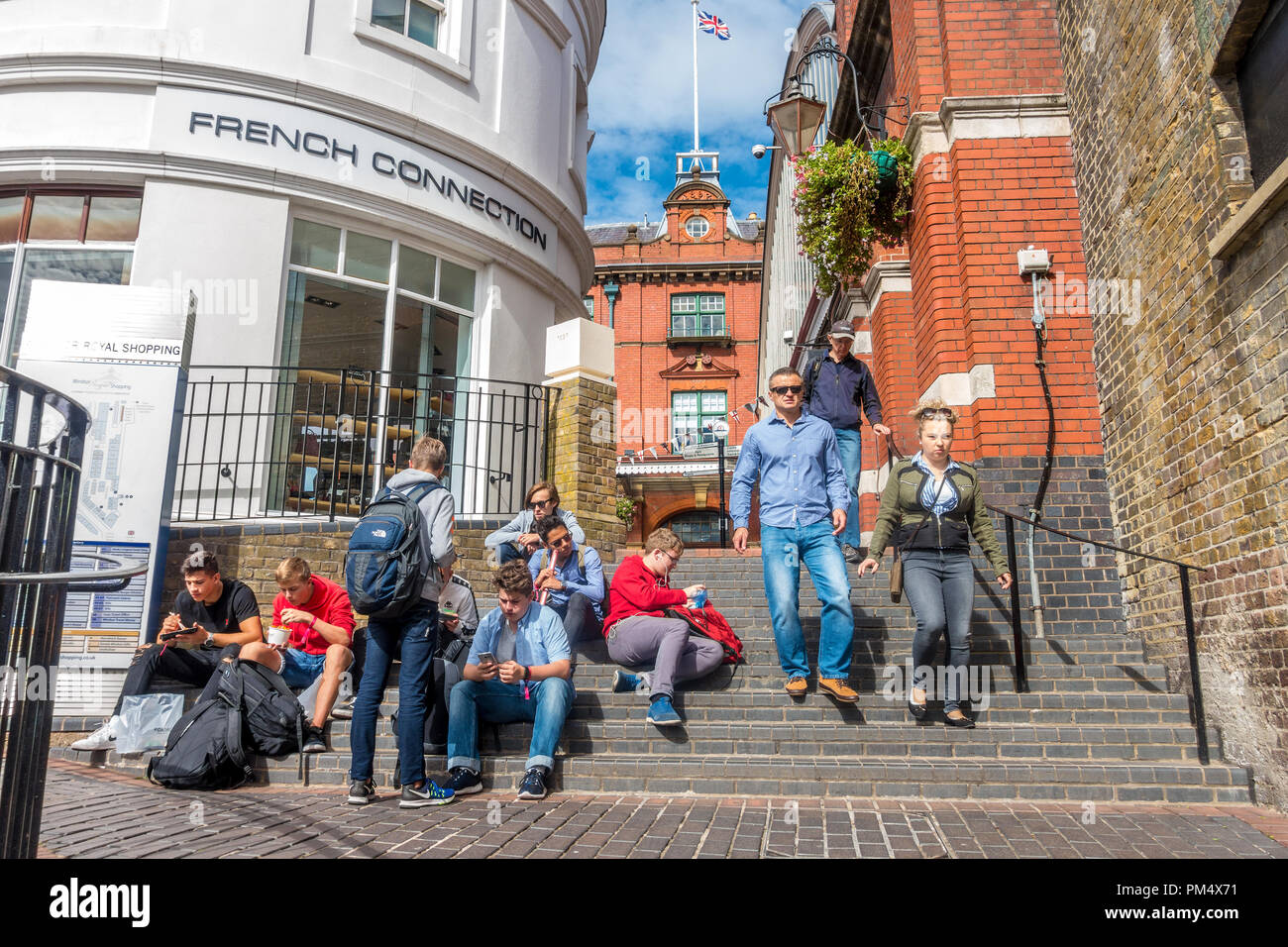 A group of young men sit on steps outside the French Connection store in Windsor, UK. Stock Photo