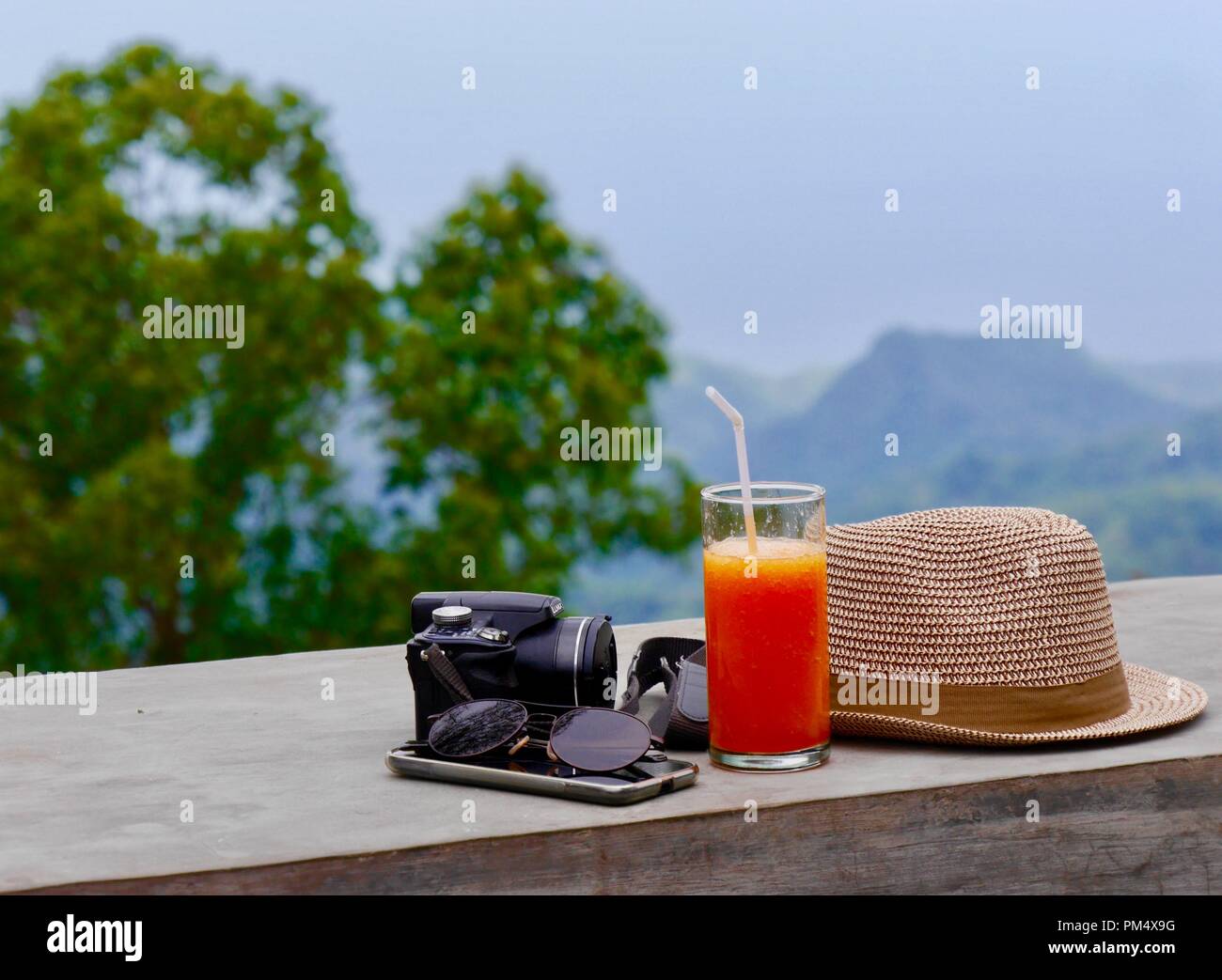Close up of travel essentials, sunhat, camera, mobile and sunglasses against background of beautiful mountainous scenery with ample editorial space Stock Photo