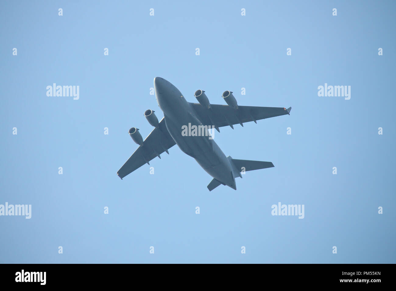 Four engine military cargo plane flying in the air. Dark gray plane silhouette with four jet engines, blue sky on the background. Stock Photo