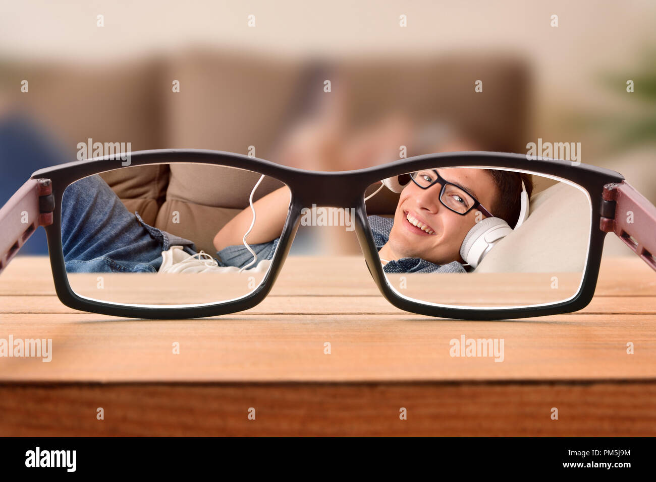 Conceptual view of visual correction with focused scene through eyeglasses of a young man with glasses entertaining lying on a sofa. Stock Photo