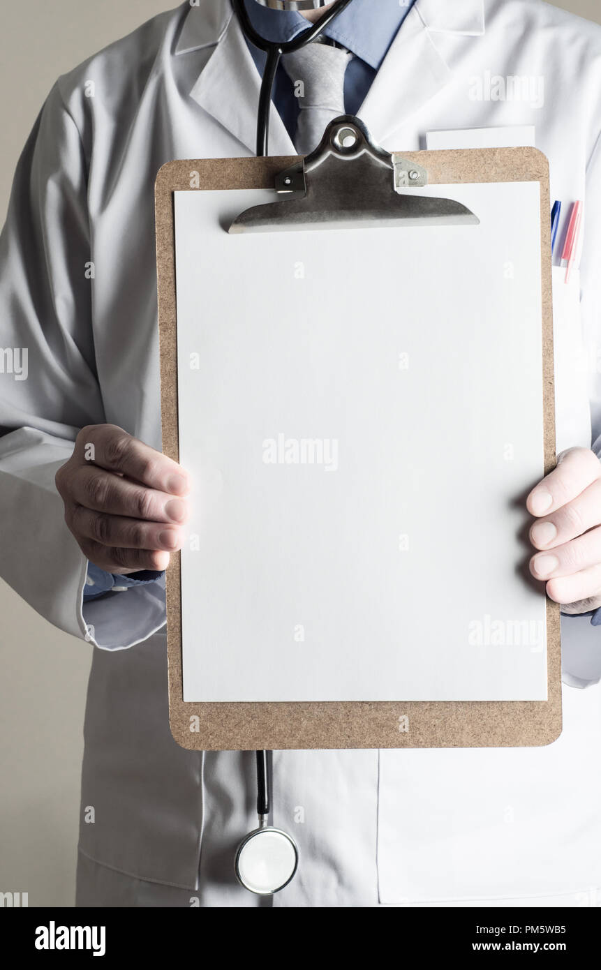 Male model dressed as Doctor. Facing front and holding up a clipboard with blank sheet of paper as a sign providing copy space for a message. Stock Photo