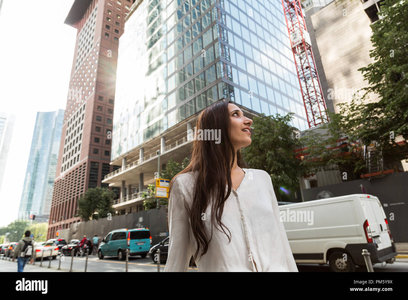Young woman standing in awe underneath skyscrapers and office buildings in an urban metropolis. Low angle view. Stock Photo
