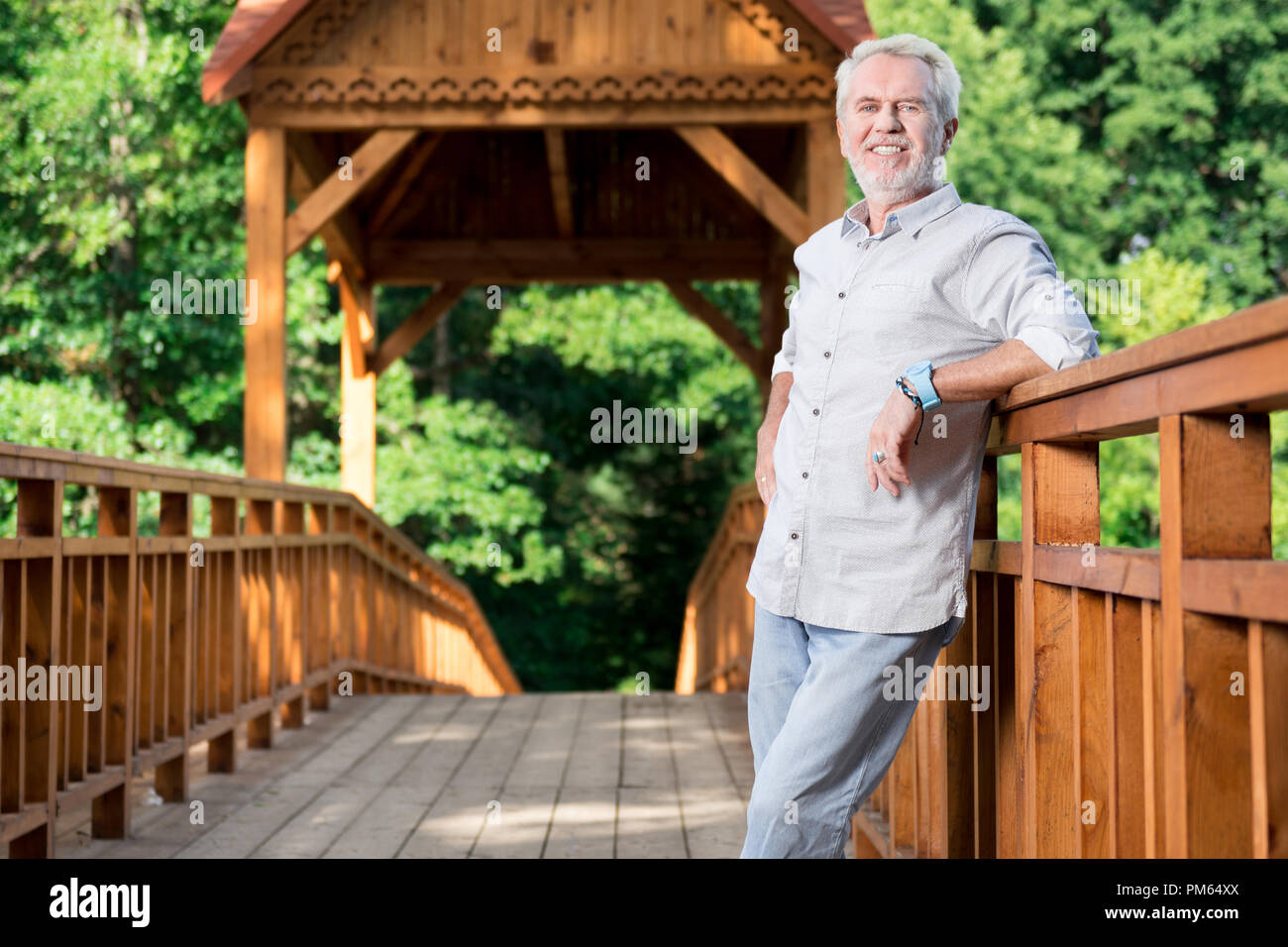 Happy aged man feeling good and smiling while standing on the bridge Stock Photo