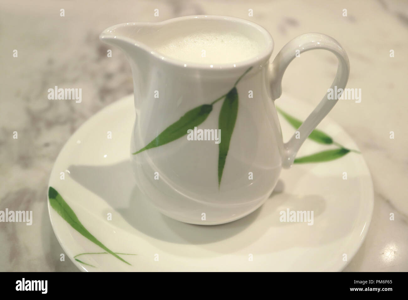 Closed up white with green pattern ceramic milk pitcher on white marble table Stock Photo