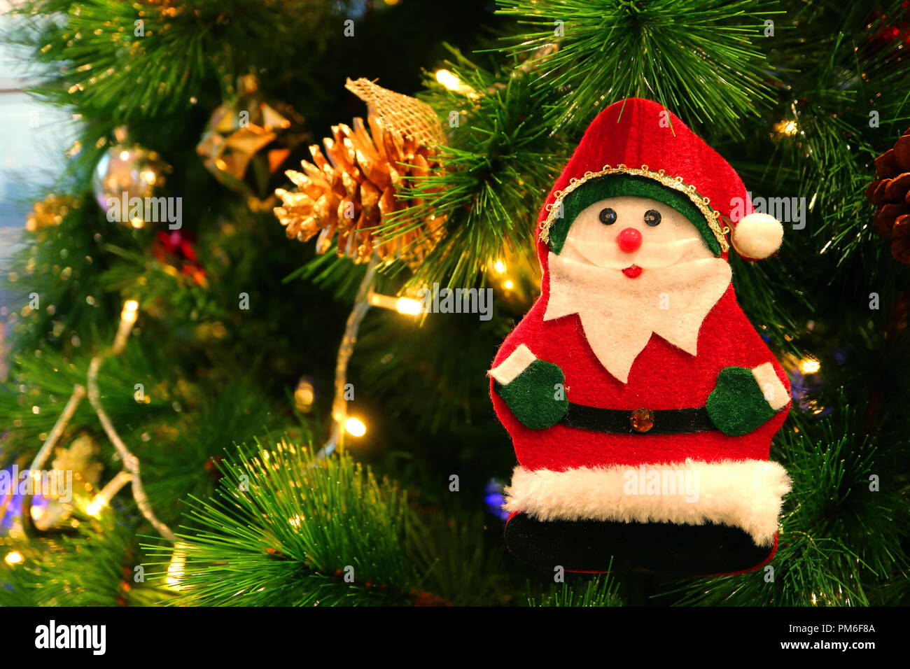 Felt Santa Claus Ornament and Gold Pine Cone Hanging on a Sparkling Christmas Tree Stock Photo