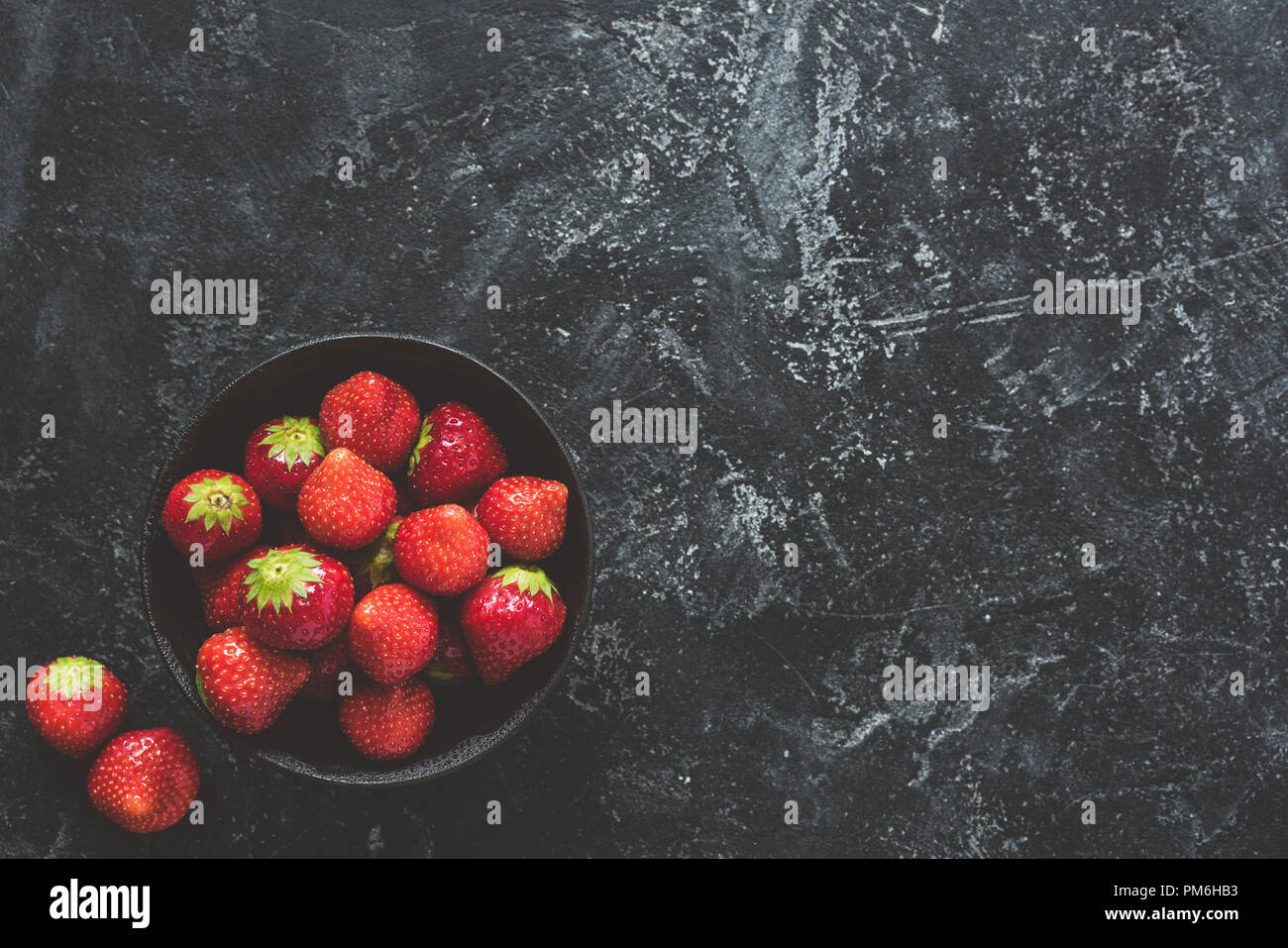 Fresh strawberries in bowl on black concrete background. Top view Stock Photo