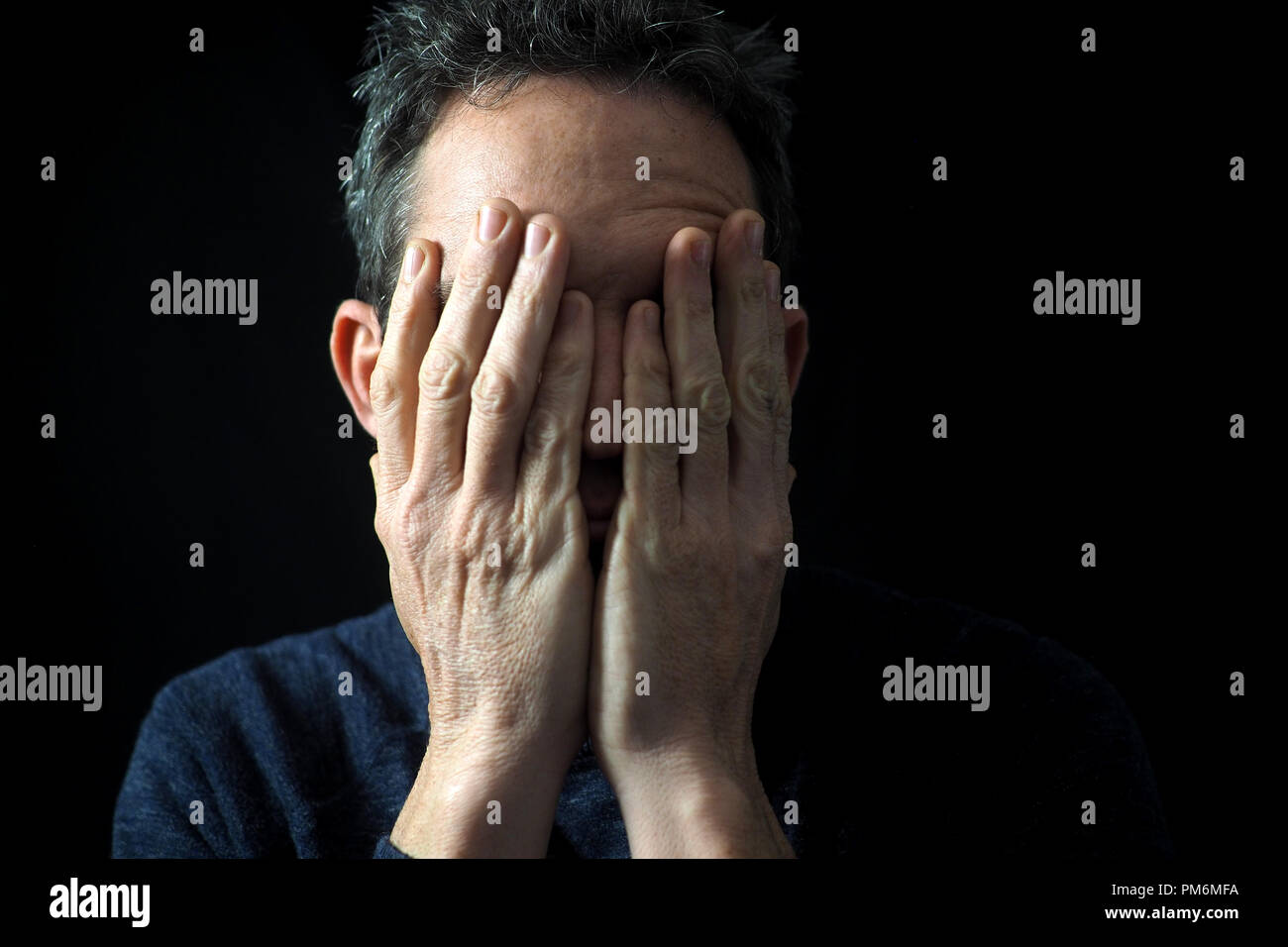 Portrait of man on black background, stressed, hands on face Stock Photo