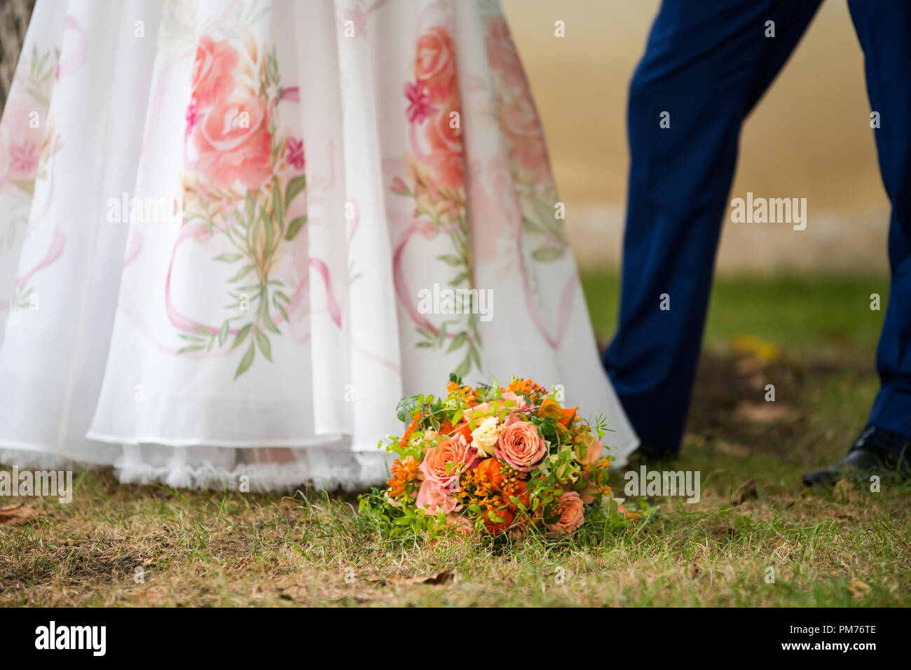on the green grass between the legs of the bride and groom lies a bouquet of wedding Stock Photo