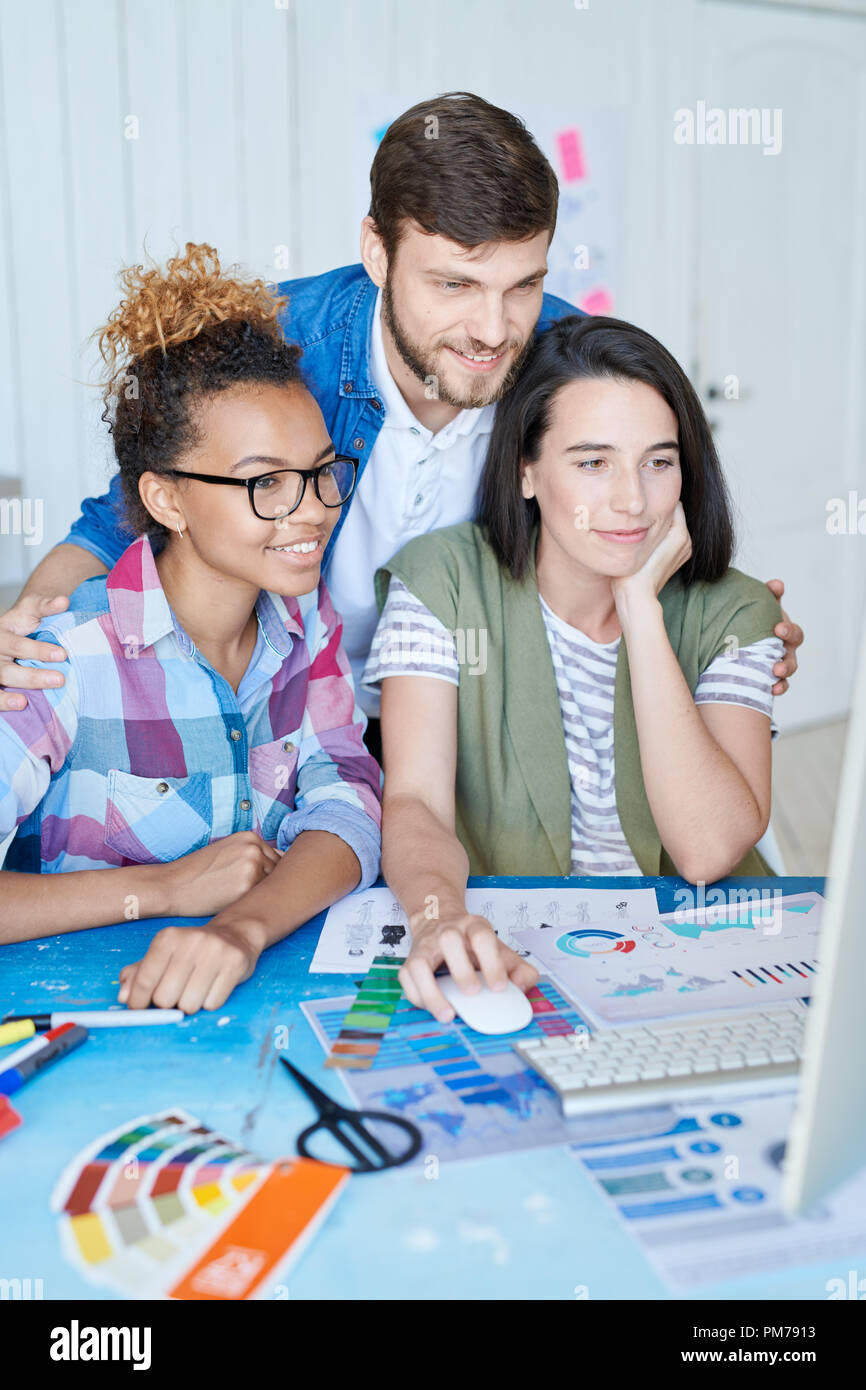 Portrait of three creative designers using computer for internet networking while working at desk in office Stock Photo