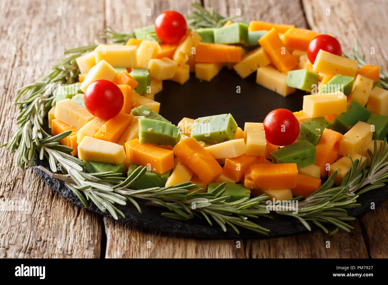 Sliced pesto cheese, cheddar, Mimolette with tomatoes and rosemary close-up on the table. Christmas decor. horizontal Stock Photo