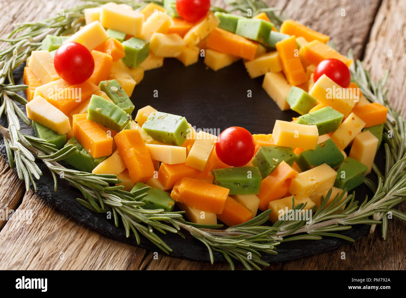 New Year's appetizer of pesto cheese, cheddar, Mimolette with tomatoes and rosemary close-up on the table. horizontal Stock Photo