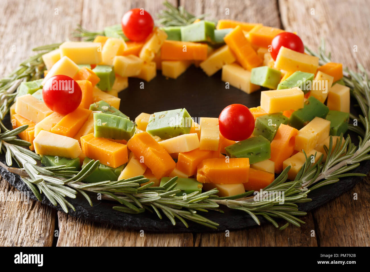 delicious Christmas set of pesto cheese, cheddar, mimolette with tomatoes and rosemary close-up on the table. horizontal Stock Photo