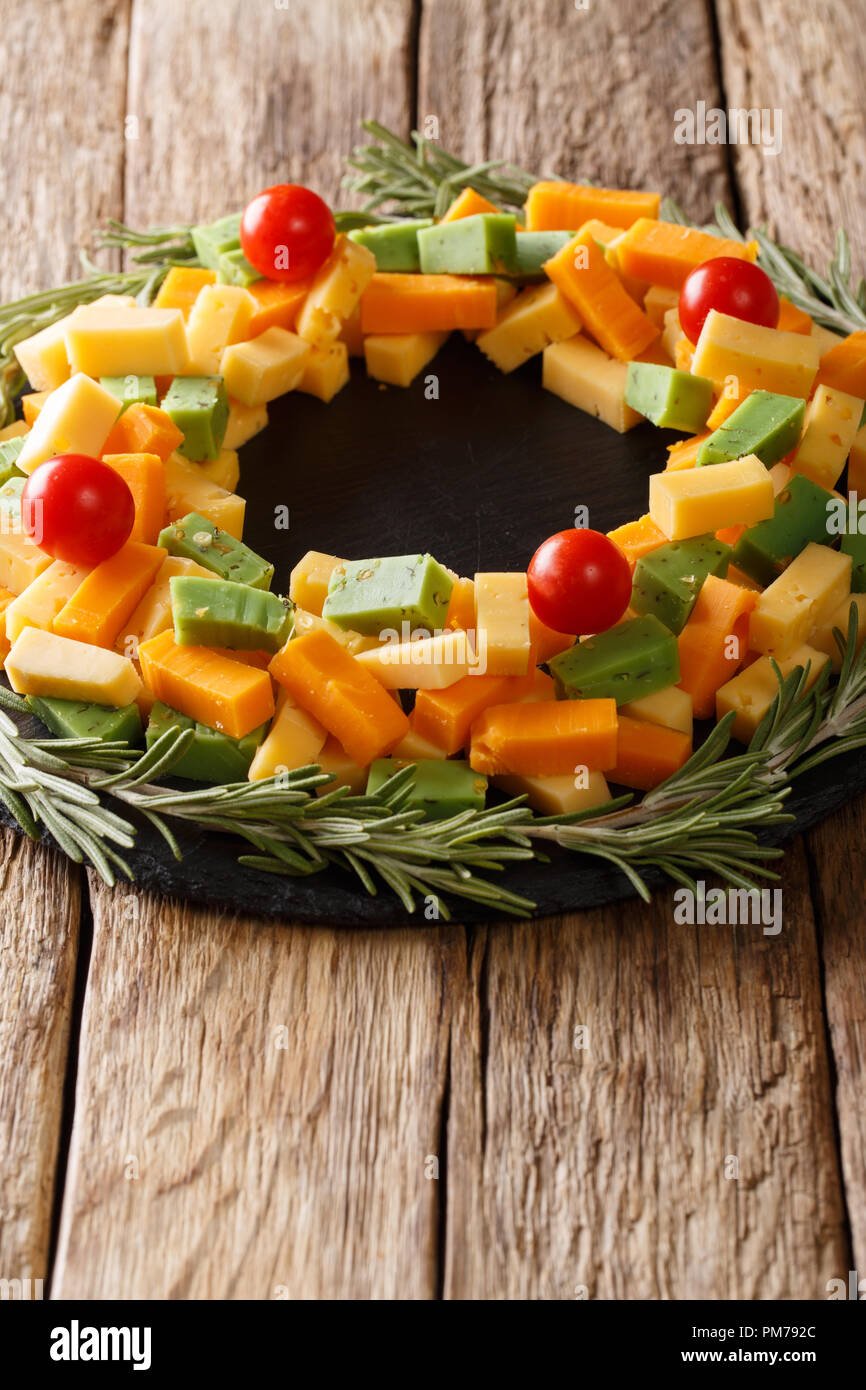 Christmas food: a wreath of pesto cheese, cheddar, mimolette with tomatoes and rosemary close-up on the table. vertical Stock Photo