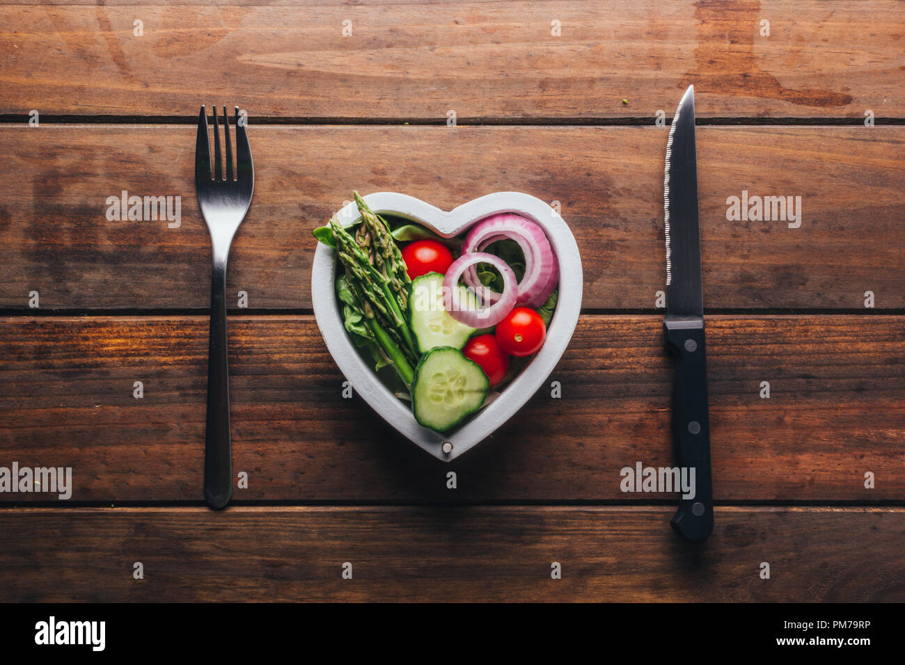 Top view of a wooden table with a plate of heart-shaped salad and its cutlery, concept of love for food Stock Photo