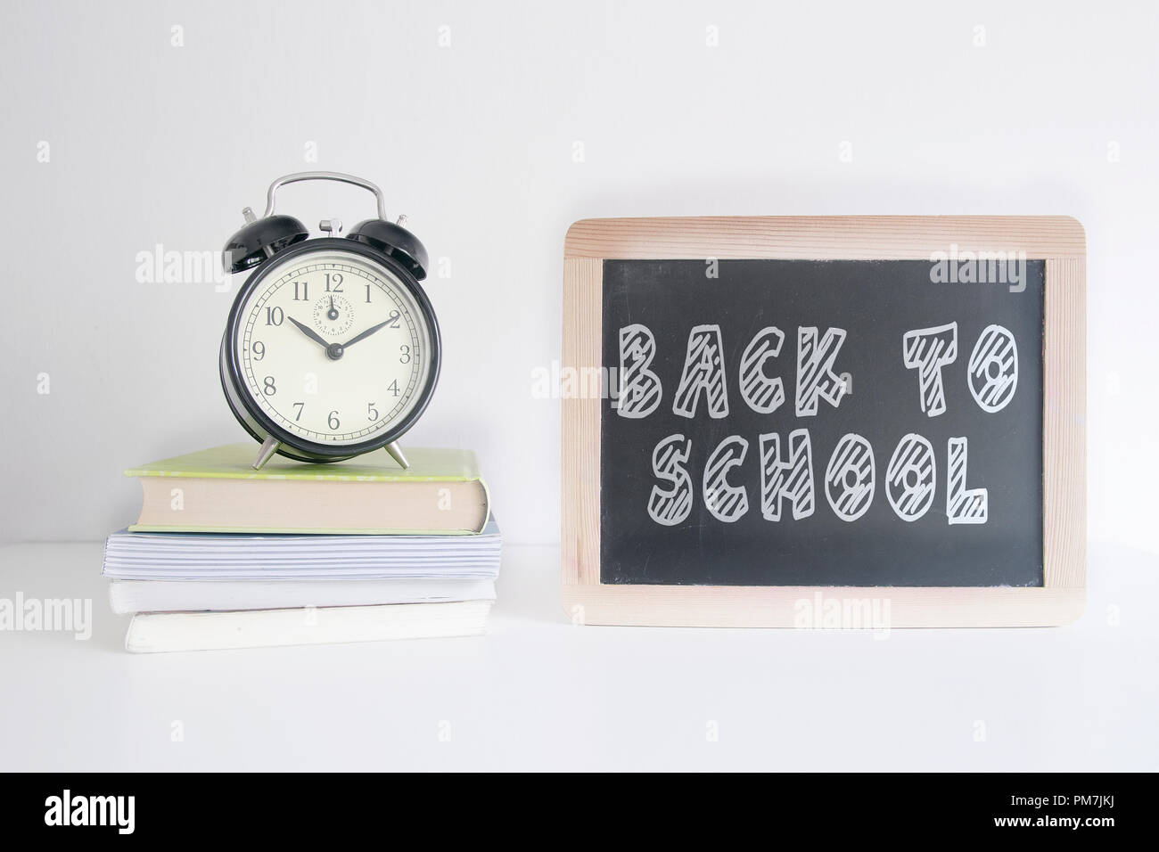 Alarm clock on a pile of books next to a blackboard with the text BACK TO SHOOL wrote on it. Empty copy space for Editor's text. Stock Photo