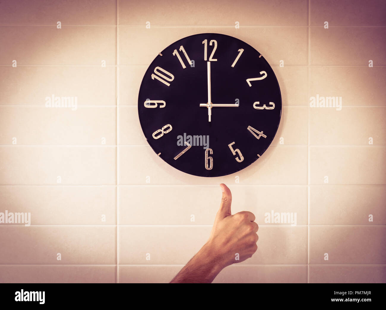 Big black clock on white wall. Time change. DST. Survey of the European Union on time change. Gesture of agreement. Thumb up of Caucasian man. Stock Photo