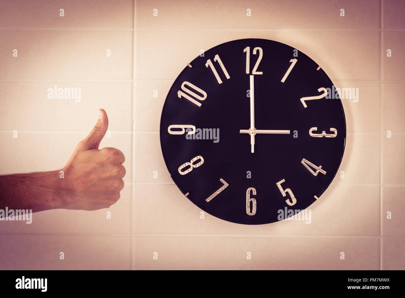 Big black clock on white wall. Time change. DST. Survey of the European Union on time change. Gesture of agreement. Thumb up of Caucasian man. Stock Photo