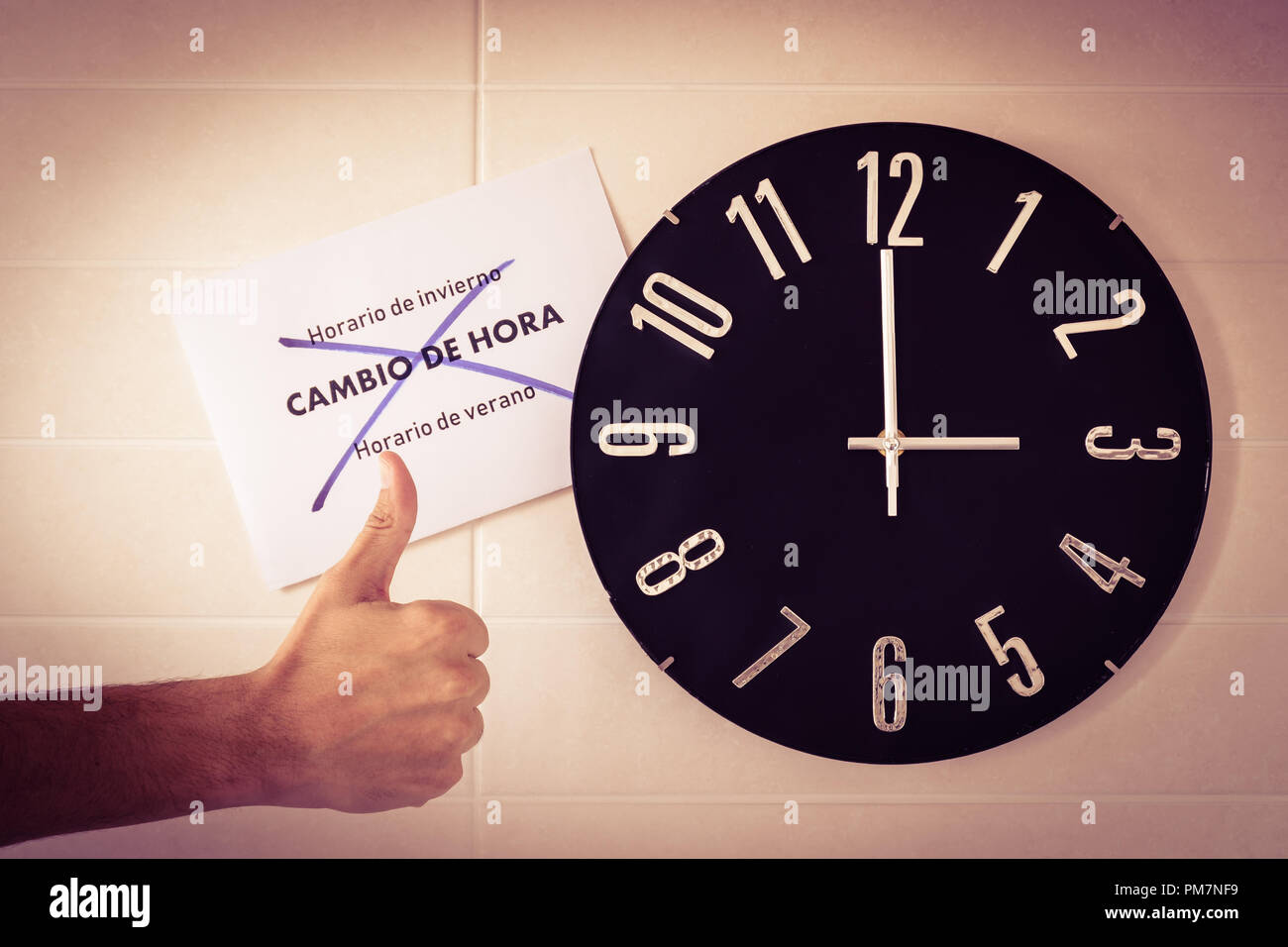 Big black clock on white wall. Time change. DST. Survey of the European Union. Gesture of agreement . Thumb up of caucasian man. Spanish banner. Stock Photo