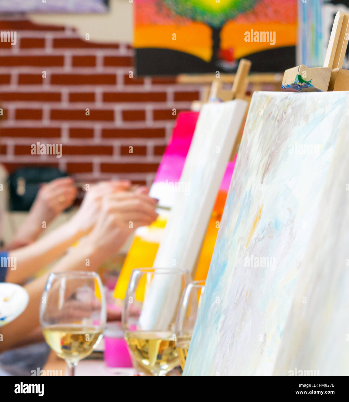 Many women of different ages drawing on canvases with brushes and drinking champagne during masterclass in the art studio, hands only Stock Photo