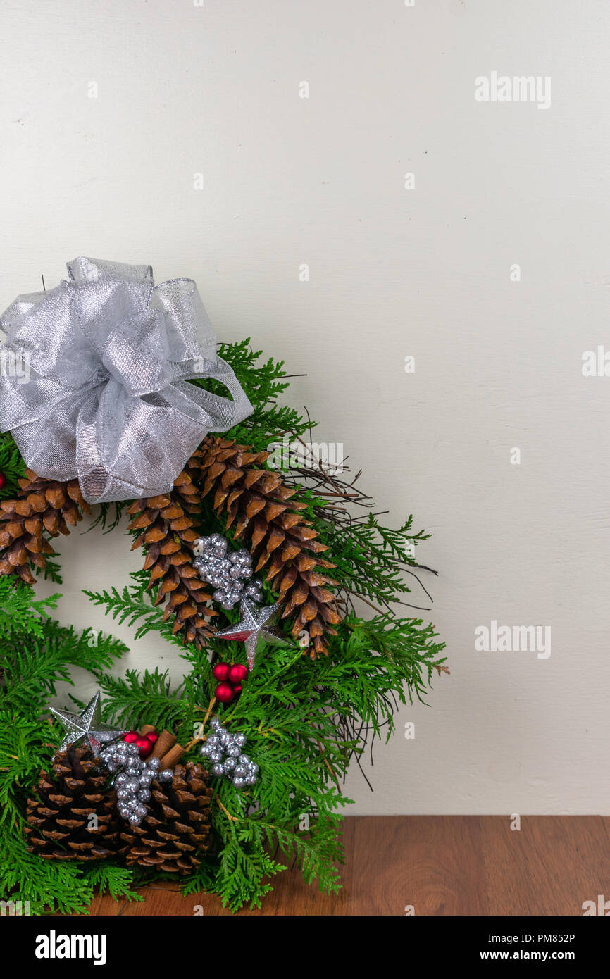 A Christmas wreath with cedar branches, pine cones, cinnamon sticks, silver  stars, red berries, and silver berry clusters with a silver bow on top Stock Photo