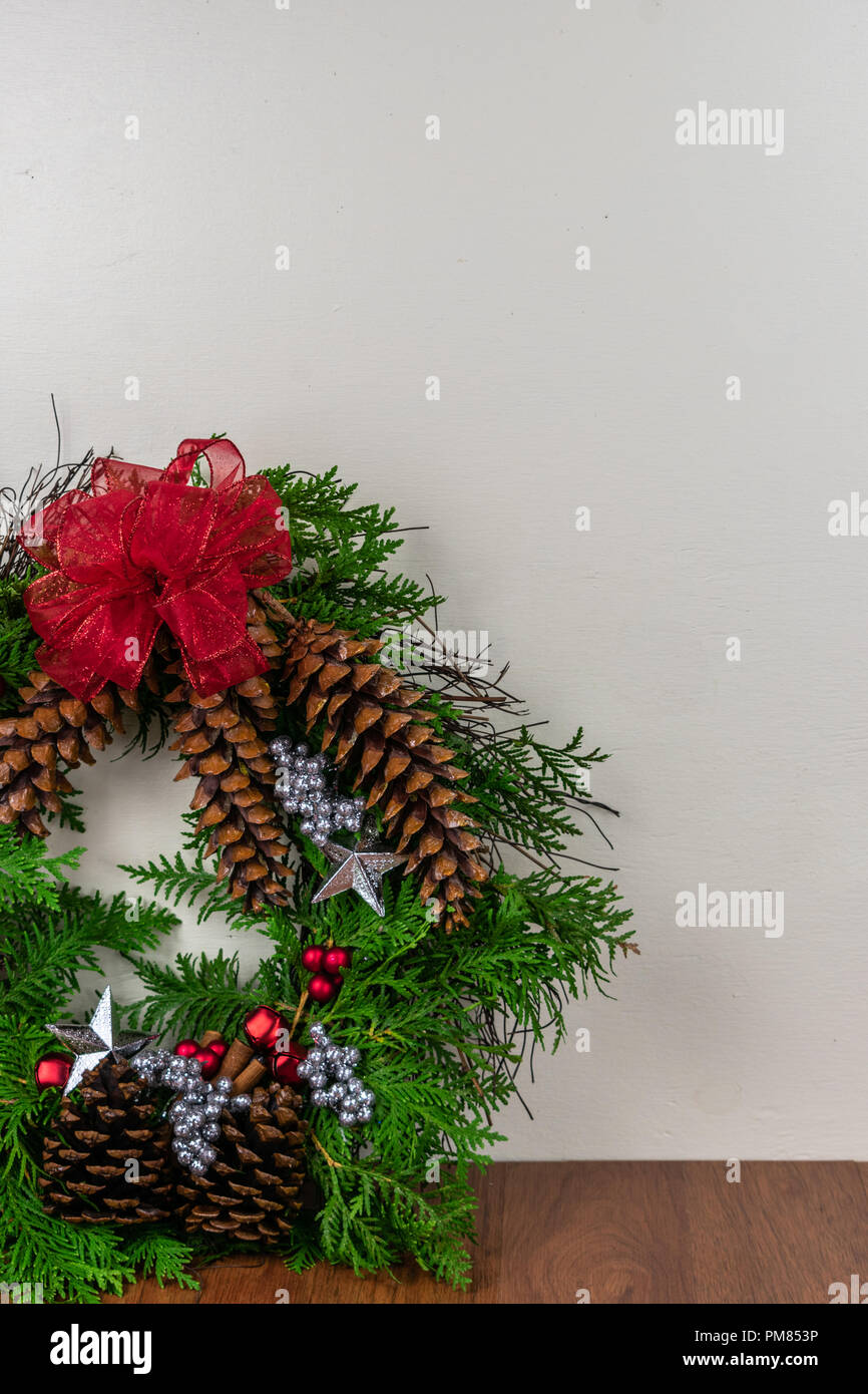 A Christmas wreath with cedar branches, pine cones, silver  stars, red bells, red berries, and silver berry clusters with a red bow on top Stock Photo