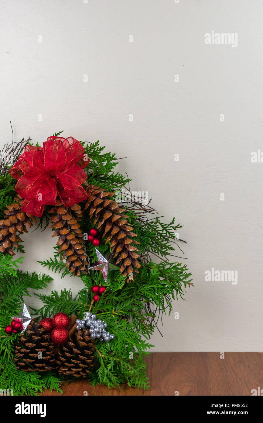 A Christmas wreath with cedar branches, pine cones, silver  stars, red ornaments,  red berries, and silver berry clusters with a red bow on top Stock Photo