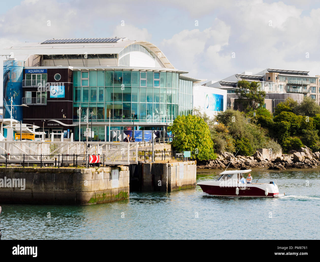 Small motor boat entering the entrance of Sutton Harbour, Plymouth, Devon, UK.  National Marine Aquarium in the background Stock Photo