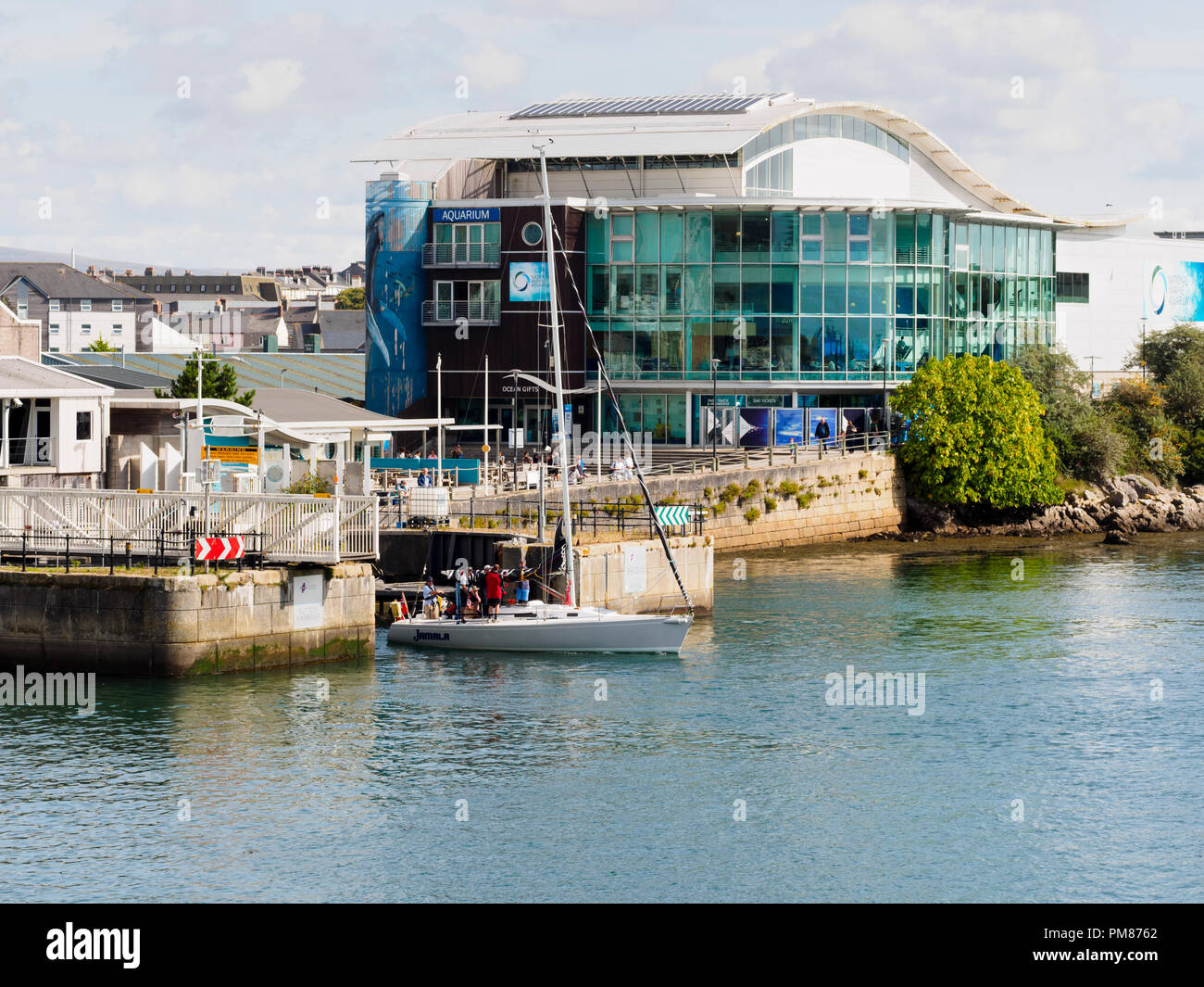 Small yacht leaving the entrance of Sutton Harbour, Plymouth, Devon, UK.  National Marine Aquarium in the background Stock Photo