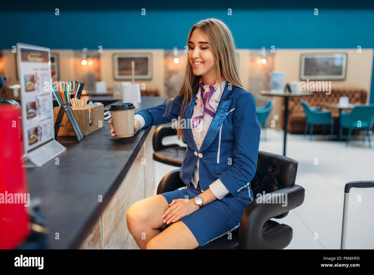 Stewardess with hand luggage drinks coffee in airport cafe. Air hostess with baggage, flight