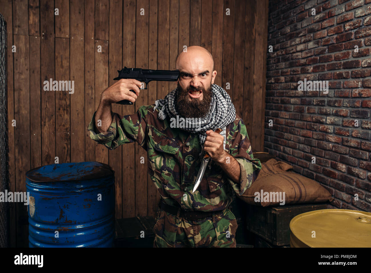 Bearded terrorist in uniform with knife and a gun at his head, male mujahedin with weapon, wahab. Terrorism and terror, soldier in khaki camouflage Stock Photo