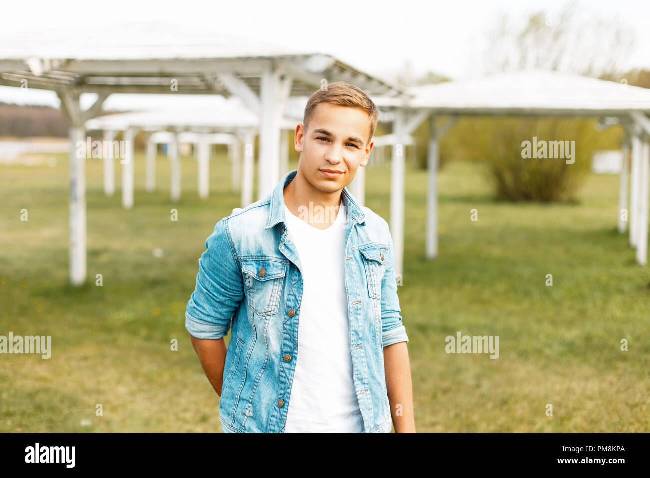 Happy young man in jeans and a white T-shirt near white canopies in the nature Stock Photo