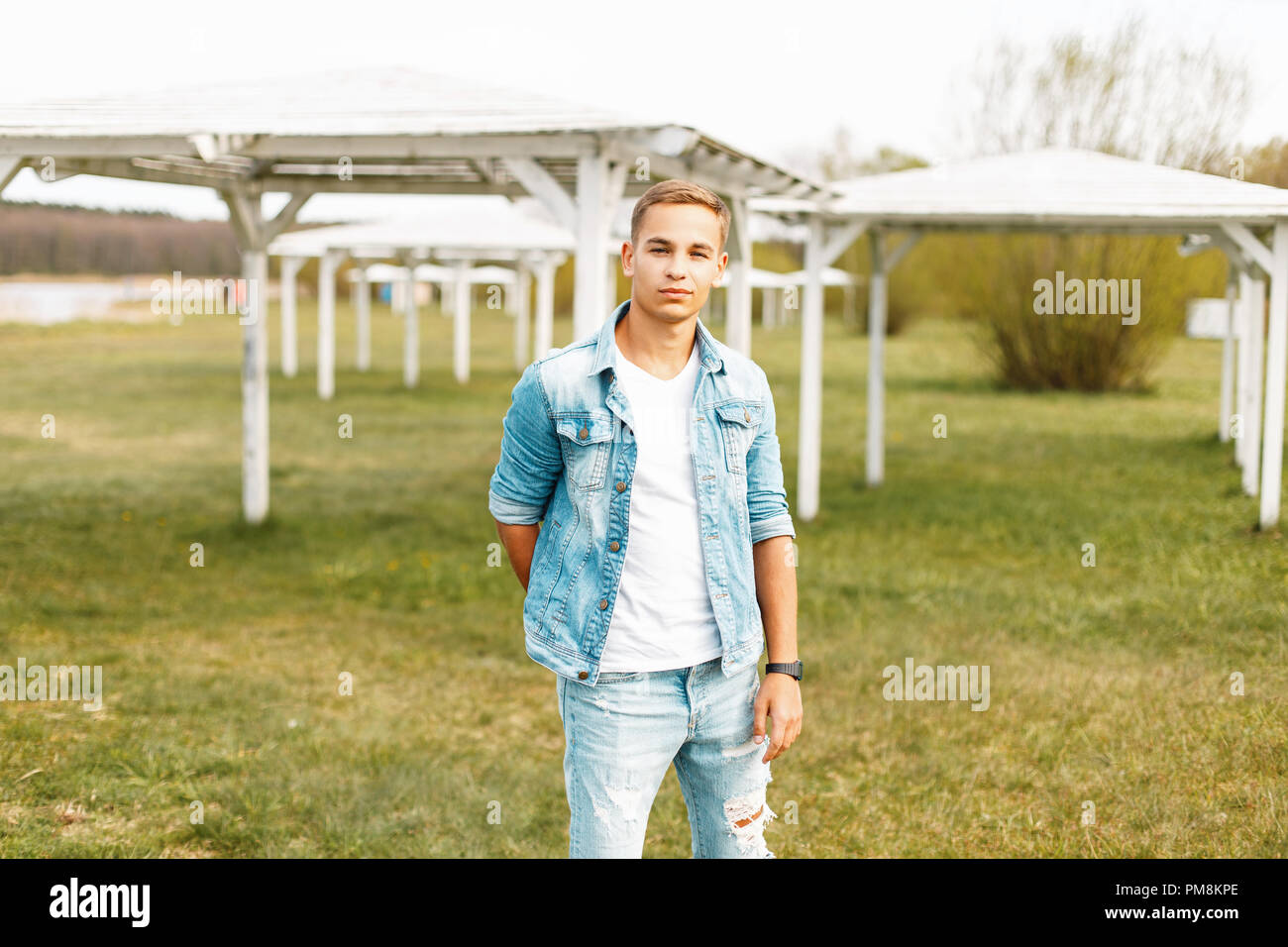 Stylish young man in a jeans jacket and jeans in a white T-shirt is resting in nature Stock Photo