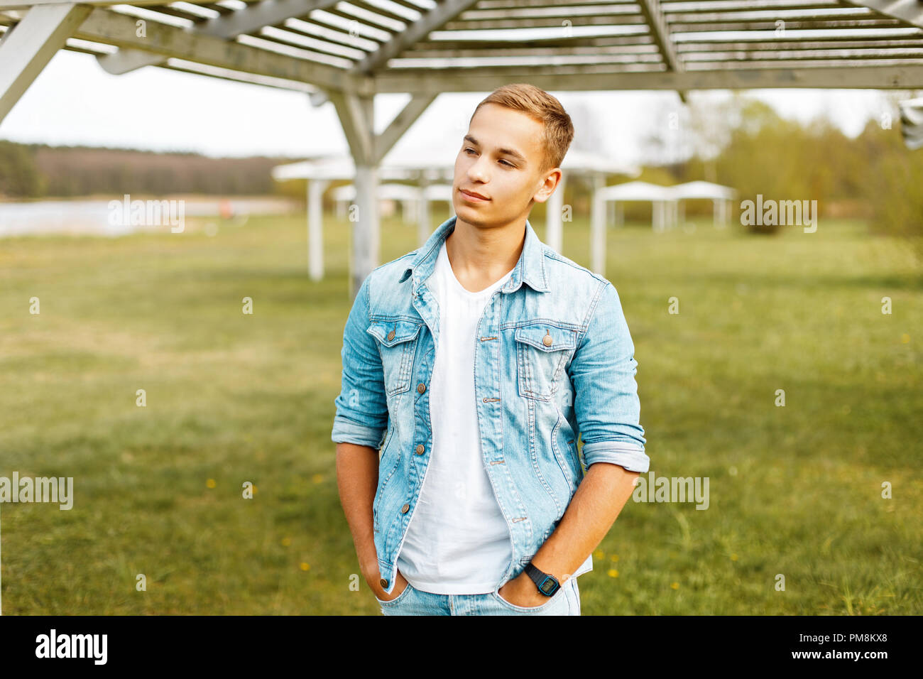 Natural portrait of a young man in a denim jacket and a white shirt near the white wooden canopy Stock Photo