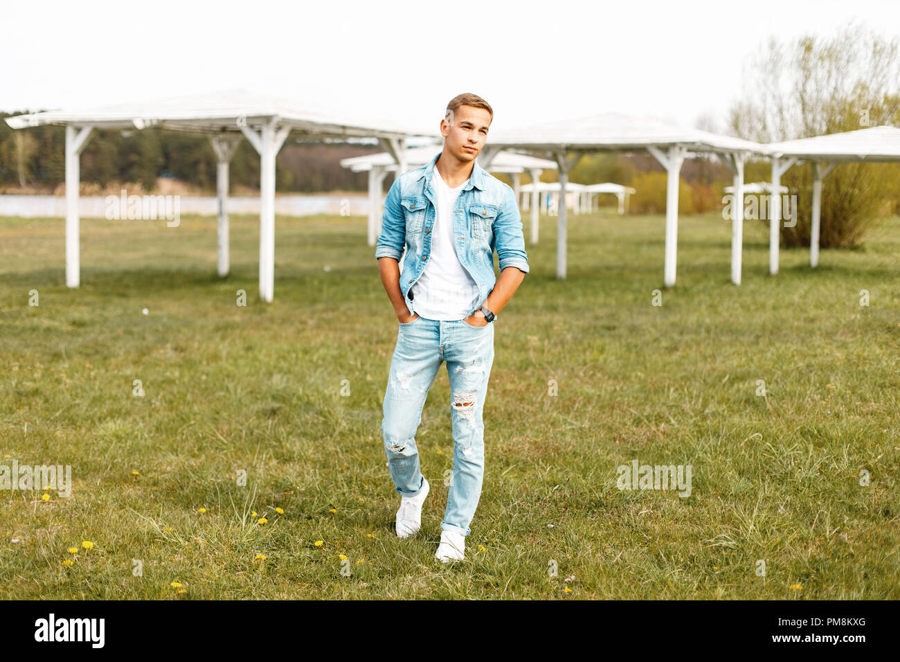 Handsome young man in a denim jacket and white T-shirt with torn jeans walking in nature Stock Photo